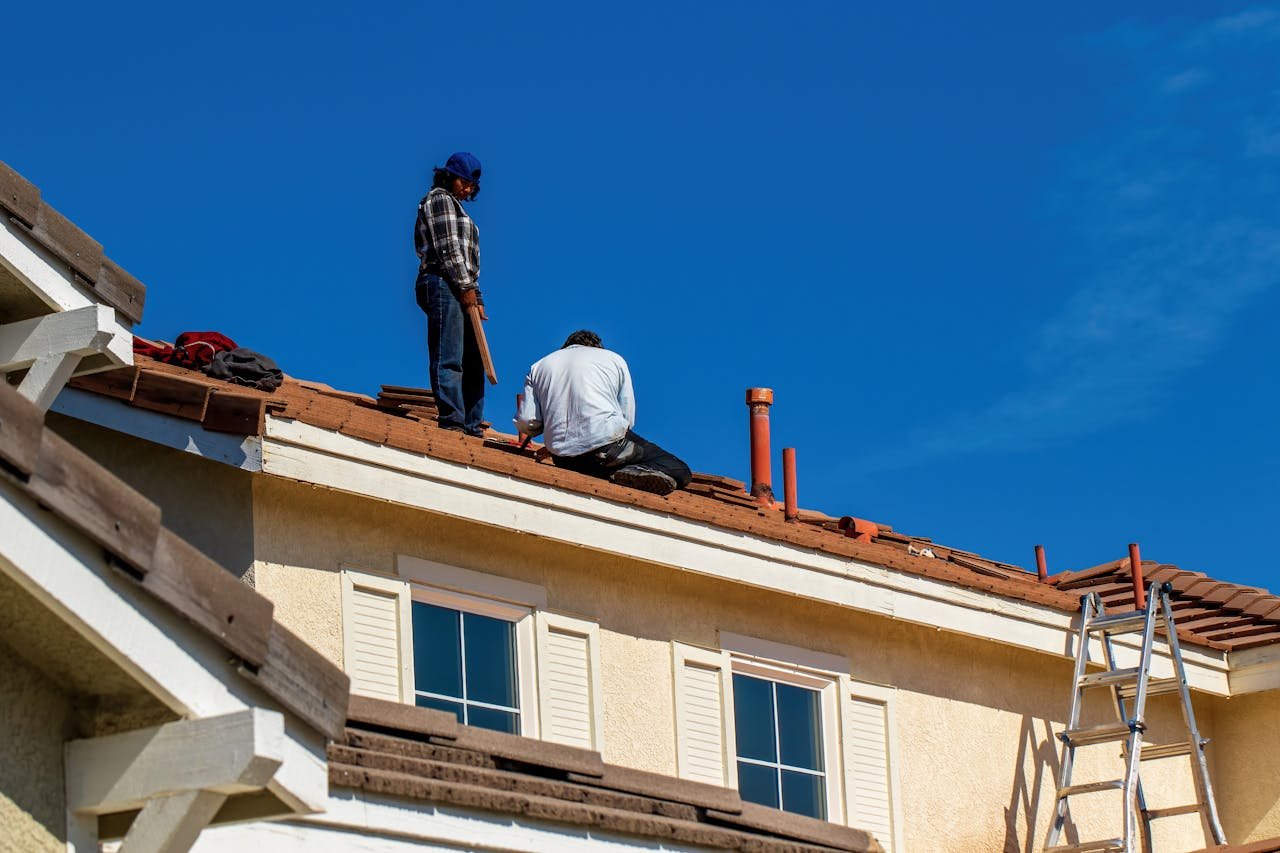hero-img-02 Roof construction scene with workers on a tiled roof, captured under a clear blue sky.