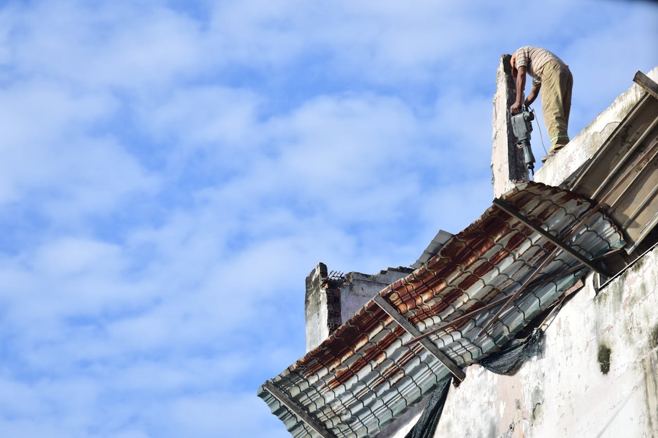 why-choose-us A construction worker using tools to demolish an old building roof against a sky background.